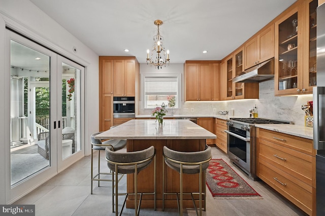 1646 Foxhall Rd NW, Washington, DC 20007 - kitchen featuring stainless steel appliances, under cabinet range hood, a chandelier, backsplash, and light stone countertops