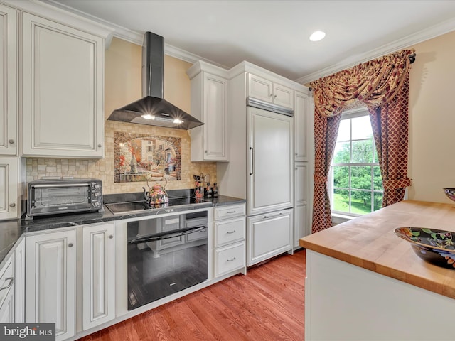 42 Bissenden Way, Reinholds, PA 17569 - kitchen with wall chimney exhaust hood, oven, black electric stovetop, light wood-style flooring, and crown molding
