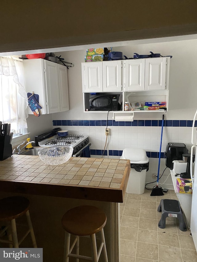 846 Windermere Ave, Drexel Hill, PA 19026 - kitchen featuring tile counters, white gas stove, a breakfast bar area, white cabinets, and a peninsula