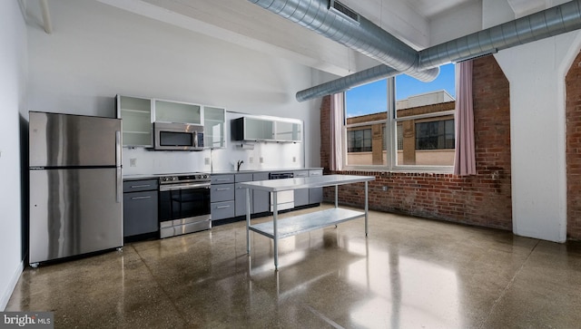 444 N 4th St Unit 401, Philadelphia, PA 19123 - kitchen featuring appliances with stainless steel finishes, brick wall, a towering ceiling, gray cabinets, and glass insert cabinets