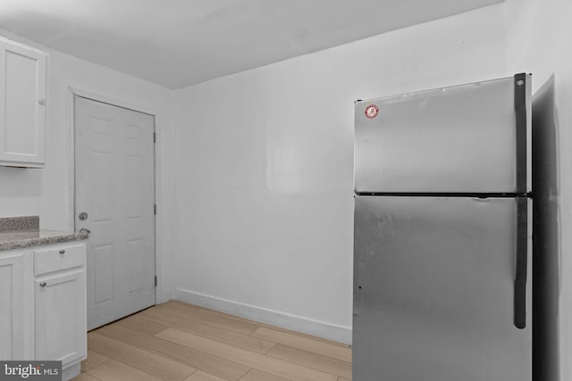 kitchen featuring freestanding refrigerator, white cabinetry, light wood finished floors, and light stone counters