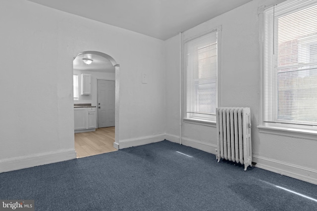 carpeted spare room featuring radiator, arched walkways, and healthy amount of natural light