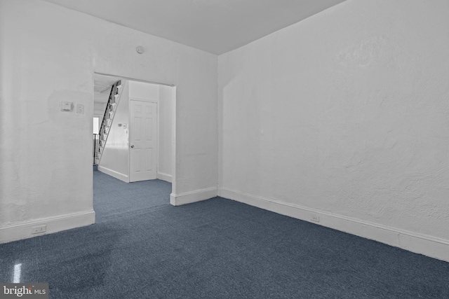 unfurnished room featuring dark carpet and baseboards