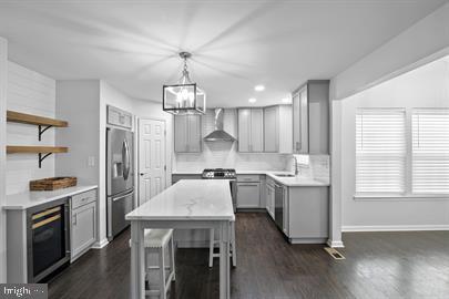 362 Harvest Grove Trl, Dover, DE 19901 - kitchen with wall chimney range hood, stainless steel appliances, gray cabinetry, wine cooler, and dark wood finished floors