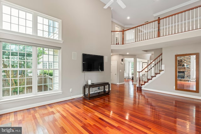 42066 Fiddlehead Pl, Aldie, VA 20105 - unfurnished living room featuring a towering ceiling, stairs, hardwood / wood-style flooring, crown molding, and a ceiling fan