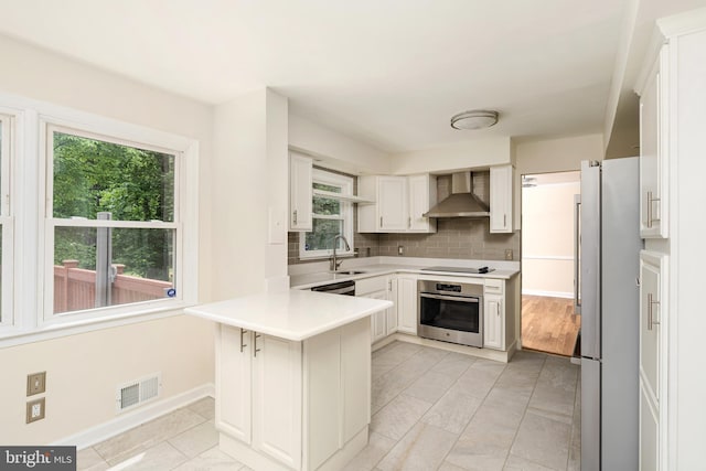76 Stonicker Dr, Lawrence, NJ 08648 - kitchen featuring appliances with stainless steel finishes, wall chimney exhaust hood, a peninsula, tasteful backsplash, and healthy amount of natural light