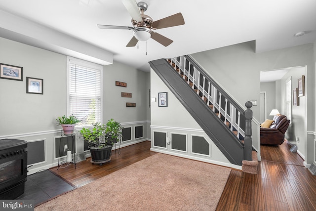 7615 Belmont Ave, Baltimore, MD 21224 - living room with a wood stove, stairs, wood finished floors, a ceiling fan, and wainscoting