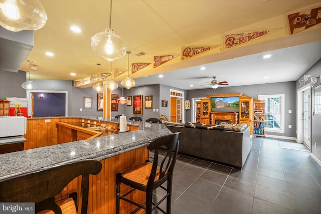 43146 Scenic Creek Way, Leesburg, VA 20176 - kitchen with light stone counters, ceiling fan, a kitchen bar, dark tile patterned flooring, and brown cabinets