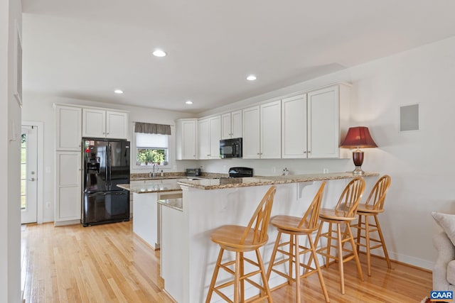 2126 Sundown Pl, Charlottesville, VA 22911 - kitchen featuring black appliances, light wood-style flooring, a peninsula, light stone countertops, and white cabinetry