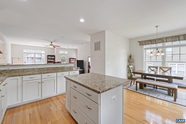 2126 Sundown Pl, Charlottesville, VA 22911 - kitchen with light wood-type flooring, a ceiling fan, white cabinets, light stone countertops, and a center island