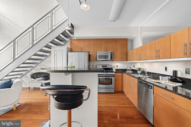 1390 Kenyon St NW Unit 524, Washington, DC 20010 - kitchen with appliances with stainless steel finishes, light wood finished floors, a kitchen island, dark stone countertops, and a breakfast bar