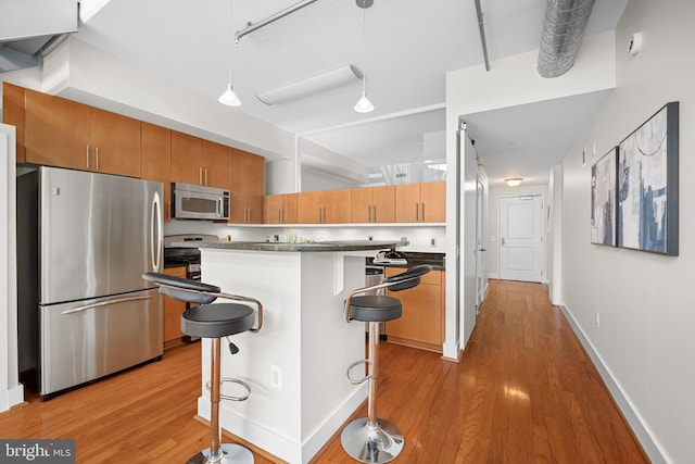 1390 Kenyon St NW Unit 524, Washington, DC 20010 - kitchen featuring appliances with stainless steel finishes, light wood-style flooring, a center island, a kitchen bar, and brown cabinets