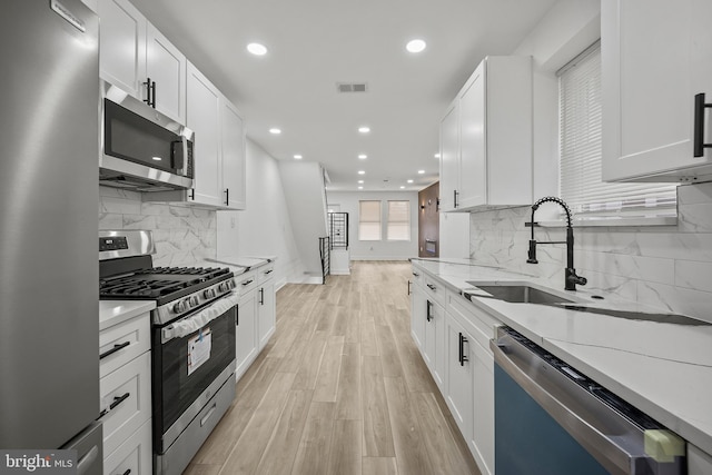 239 Rubicam St, Philadelphia, PA 19120 - kitchen with stainless steel appliances, recessed lighting, light wood-style flooring, white cabinetry, and backsplash