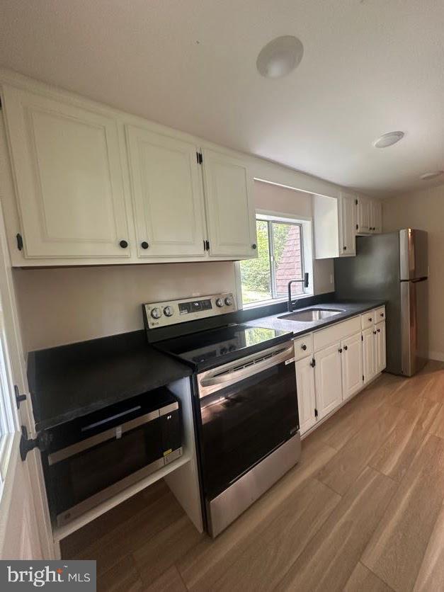 556 Trapper Ridge Ln, Hedgesville, WV 25427 - kitchen featuring stainless steel appliances, light wood finished floors, dark countertops, and white cabinetry