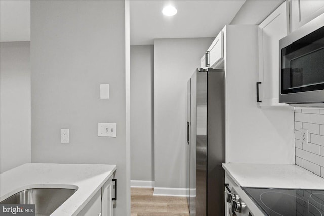 1801 Calvert St NW Unit 204, Washington, DC 20009 - kitchen with appliances with stainless steel finishes, white cabinetry, light wood-style floors, tasteful backsplash, and light stone countertops
