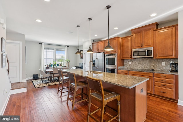 9924 Whitemoss Dr, Manassas, VA 20109 - kitchen featuring appliances with stainless steel finishes, brown cabinetry, a breakfast bar, an island with sink, and light stone countertops