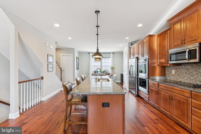 9924 Whitemoss Dr, Manassas, VA 20109 - kitchen featuring appliances with stainless steel finishes, a kitchen breakfast bar, backsplash, brown cabinetry, and a kitchen island with sink