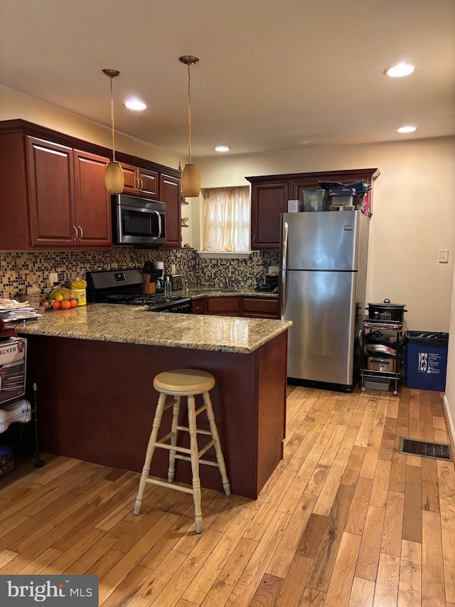 2739 W Harper St W, Philadelphia, PA 19130 - kitchen featuring stainless steel appliances, a peninsula, light wood-style floors, hanging light fixtures, and backsplash