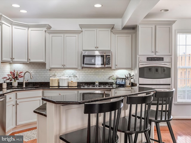 15164 Santander Dr, Gainesville, VA 20155 - kitchen featuring stainless steel appliances, a kitchen breakfast bar, dark stone countertops, decorative backsplash, and light wood finished floors