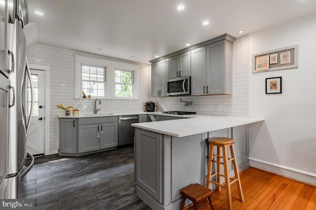 2416 Whitby Rd, Havertown, PA 19083 - kitchen featuring appliances with stainless steel finishes, gray cabinets, a peninsula, dark wood-type flooring, and a breakfast bar