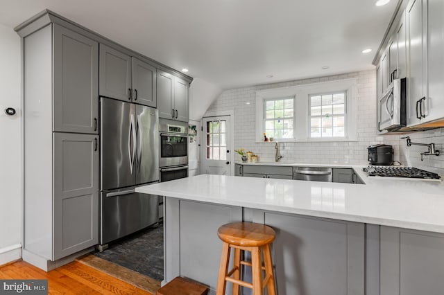 2416 Whitby Rd, Havertown, PA 19083 - kitchen with stainless steel appliances, gray cabinetry, a peninsula, wood finished floors, and tasteful backsplash