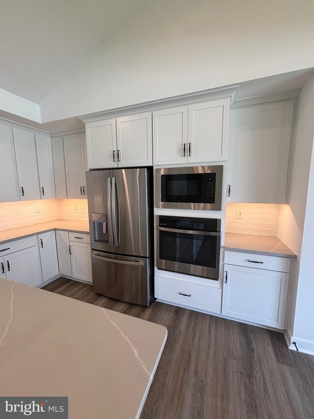 36821 W Old Gate Dr, Georgetown, DE 19947 - kitchen with stainless steel appliances, dark wood-style floors, vaulted ceiling, white cabinets, and decorative backsplash