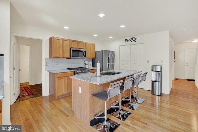1765 Ivy Pump Ln, York, PA 17408 - kitchen with stainless steel appliances, light wood-style flooring, a center island with sink, a breakfast bar area, and light stone counters