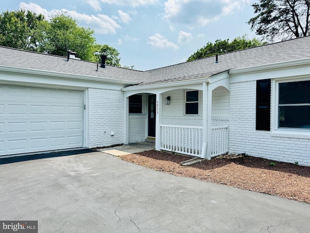 5933 Westridge Ct, Alexandria, VA 22310 - view of exterior entry featuring brick siding, covered porch, an attached garage, a shingled roof, and driveway