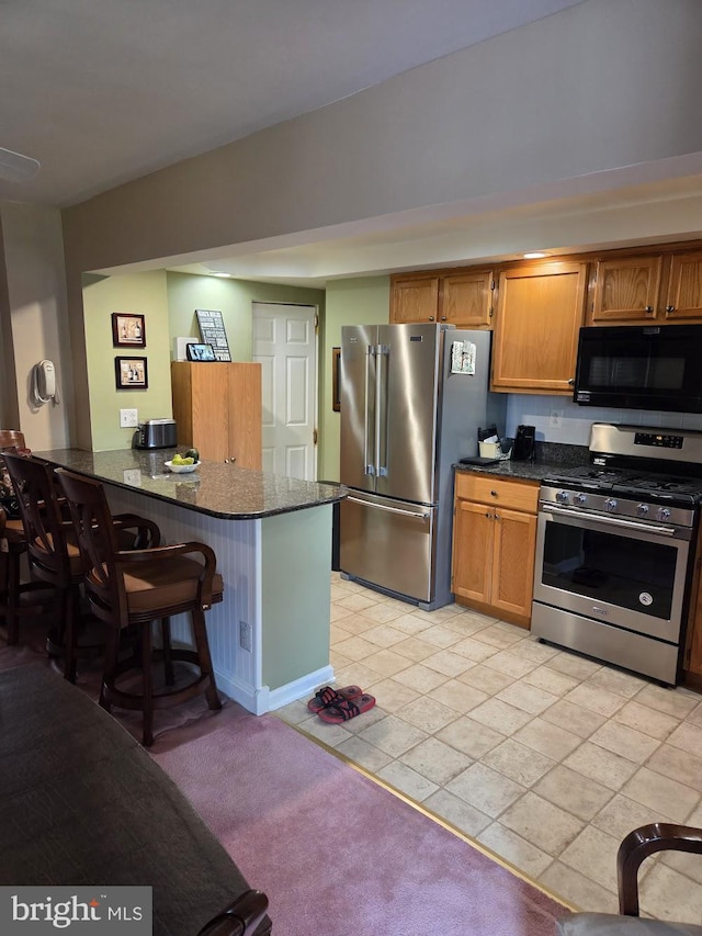 6132 Charles St, Philadelphia, PA 19135 - kitchen with stainless steel appliances, a kitchen breakfast bar, dark stone counters, a peninsula, and brown cabinetry