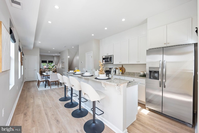 19 N Smallwood St, Baltimore, MD 21223 - kitchen with appliances with stainless steel finishes, light wood-style floors, white cabinetry, light stone countertops, and a breakfast bar