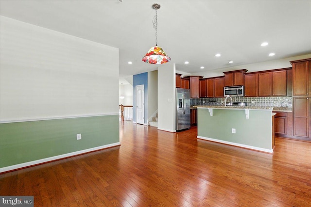 7003 Dannfield Ct, Glen Burnie, MD 21060 - kitchen with stainless steel appliances, a breakfast bar, backsplash, wood finished floors, and a center island with sink