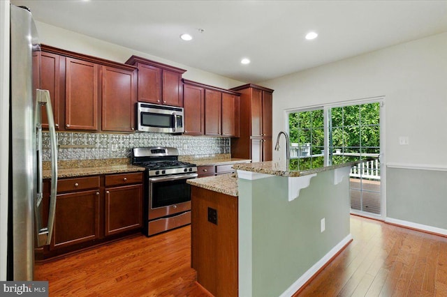 7003 Dannfield Ct, Glen Burnie, MD 21060 - kitchen featuring stainless steel appliances, wood finished floors, tasteful backsplash, a center island with sink, and light stone counters