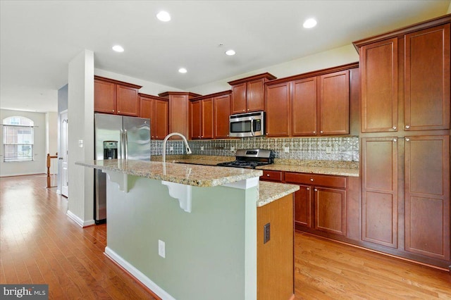 7003 Dannfield Ct, Glen Burnie, MD 21060 - kitchen featuring stainless steel appliances, light wood-style flooring, decorative backsplash, an island with sink, and light stone countertops
