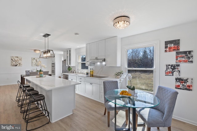 17105 Amity Dr, Derwood, MD 20855 - kitchen with a kitchen island, a chandelier, under cabinet range hood, a kitchen breakfast bar, and light wood-style flooring