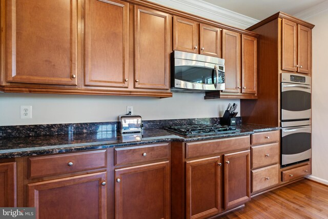500 Overlook Park Drive 27, Oxon Hill, MD 20745 - kitchen featuring stainless steel appliances, light wood finished floors, ornamental molding, brown cabinets, and dark stone counters