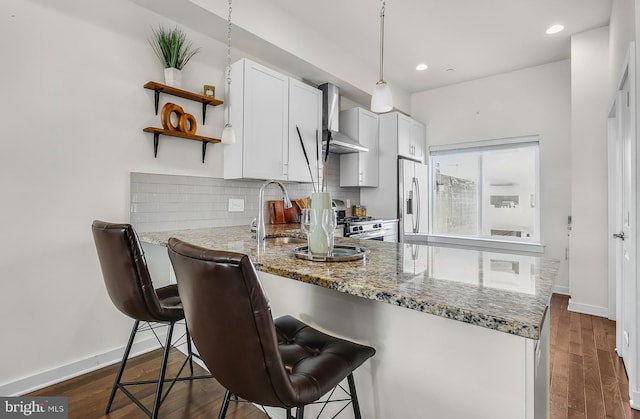 1620 N 5th Ct, Philadelphia, PA 19122 - kitchen with wall chimney range hood, stainless steel appliances, light stone counters, decorative backsplash, and a peninsula