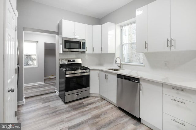 2332 N 25th St, Philadelphia, PA 19132 - kitchen featuring stainless steel appliances, light wood finished floors, white cabinetry, and tasteful backsplash