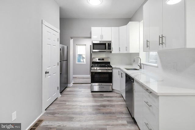 2332 N 25th St, Philadelphia, PA 19132 - kitchen featuring appliances with stainless steel finishes, white cabinetry, tasteful backsplash, and light wood-type flooring