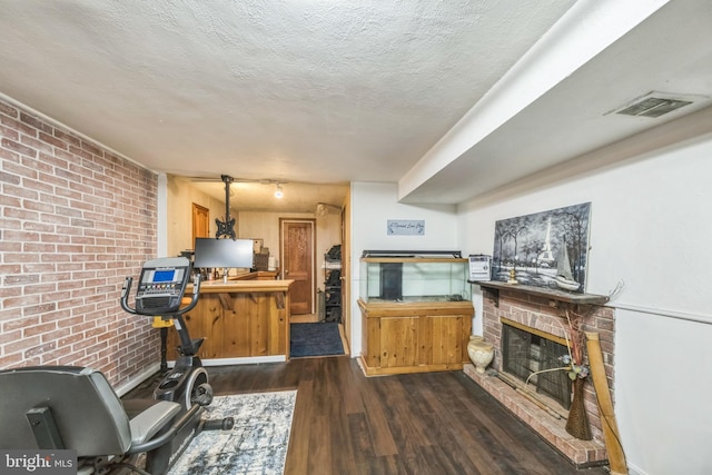 712 Chesapeake St SE, Washington, DC 20032 - living room featuring dark wood-style flooring, a fireplace with raised hearth, brick wall, and a textured ceiling