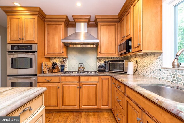 760 Audubon Dr, North Wales, PA 19454 - kitchen featuring wall chimney range hood, appliances with stainless steel finishes, light wood-type flooring, brown cabinets, and tasteful backsplash