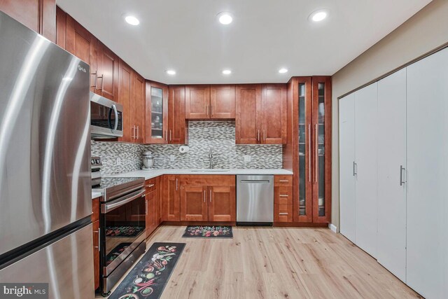 6614 Mccahill Dr, Laurel, MD 20707 - kitchen with appliances with stainless steel finishes, light wood-style floors, light countertops, backsplash, and glass insert cabinets