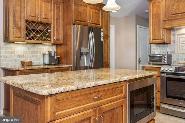 1043 Welsh Ayres Way, Downingtown, PA 19335 - kitchen with appliances with stainless steel finishes, light stone counters, brown cabinetry, and decorative backsplash