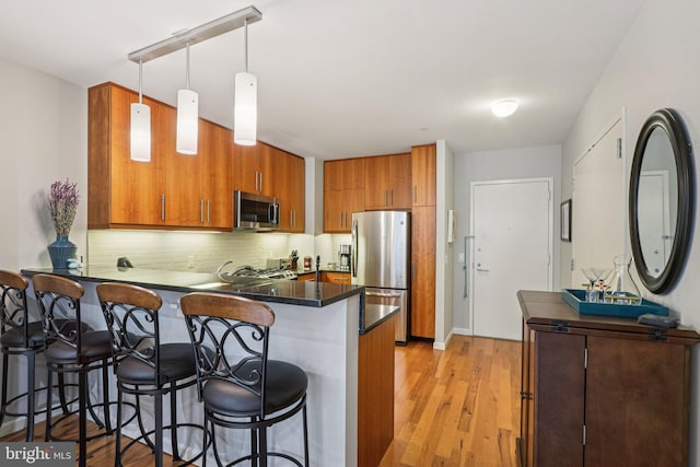 1425 Locust St Unit 7D, Philadelphia, PA 19102 - kitchen featuring appliances with stainless steel finishes, brown cabinetry, a peninsula, and a kitchen bar