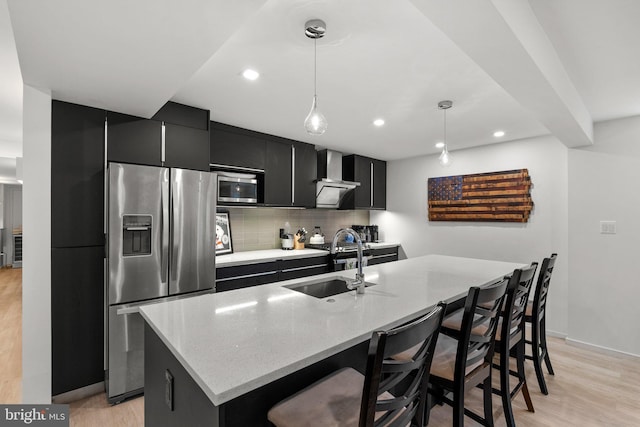 2815 39th St NW, Washington, DC 20007 - kitchen with stainless steel appliances, dark cabinetry, wall chimney exhaust hood, backsplash, and light wood-style flooring