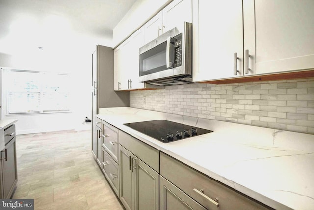 7809 Heatherton Ln, Potomac, MD 20854 - kitchen featuring stainless steel microwave, black electric cooktop, light stone countertops, tasteful backsplash, and white cabinetry