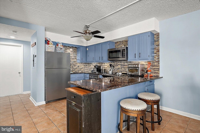 14 136th St Unit 101, Ocean City, MD 21842 - kitchen with stainless steel appliances, a peninsula, light tile patterned floors, blue cabinets, and tasteful backsplash