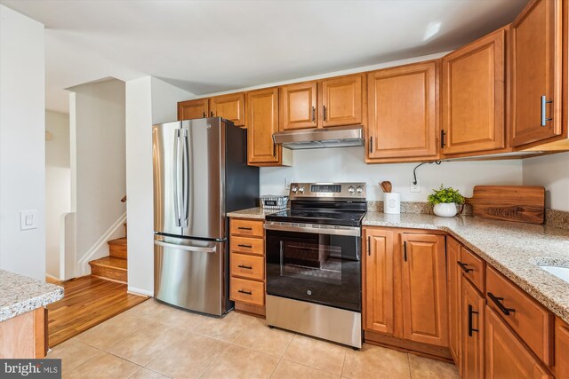 4376 Rock Ct, Waldorf, MD 20602 - kitchen featuring stainless steel appliances, under cabinet range hood, brown cabinets, light tile patterned flooring, and light stone countertops