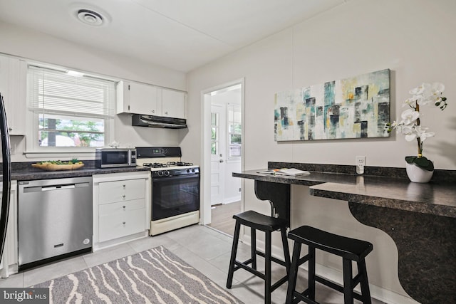 8328 Merrymount Dr, Baltimore, MD 21244 - kitchen featuring appliances with stainless steel finishes, under cabinet range hood, dark countertops, white cabinetry, and light tile patterned floors