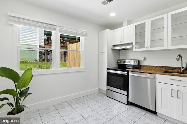 13727 Mahoney Dr, Woodbridge, VA 22193 - kitchen with stainless steel appliances, under cabinet range hood, white cabinets, glass insert cabinets, and light tile patterned flooring