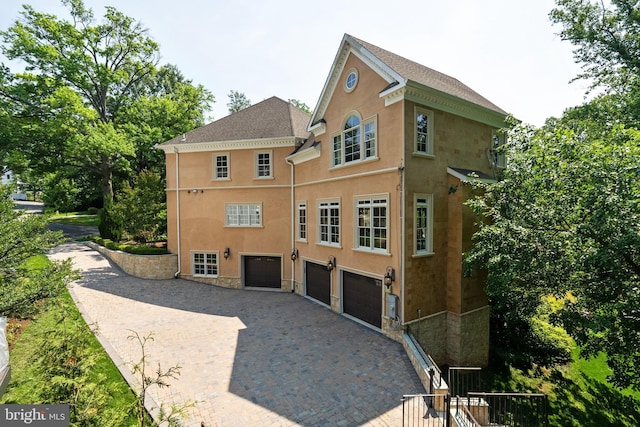 3801 52nd St NW, Washington, DC 20016 - back of house featuring a garage, stone siding, decorative driveway, stucco siding, and roof with shingles